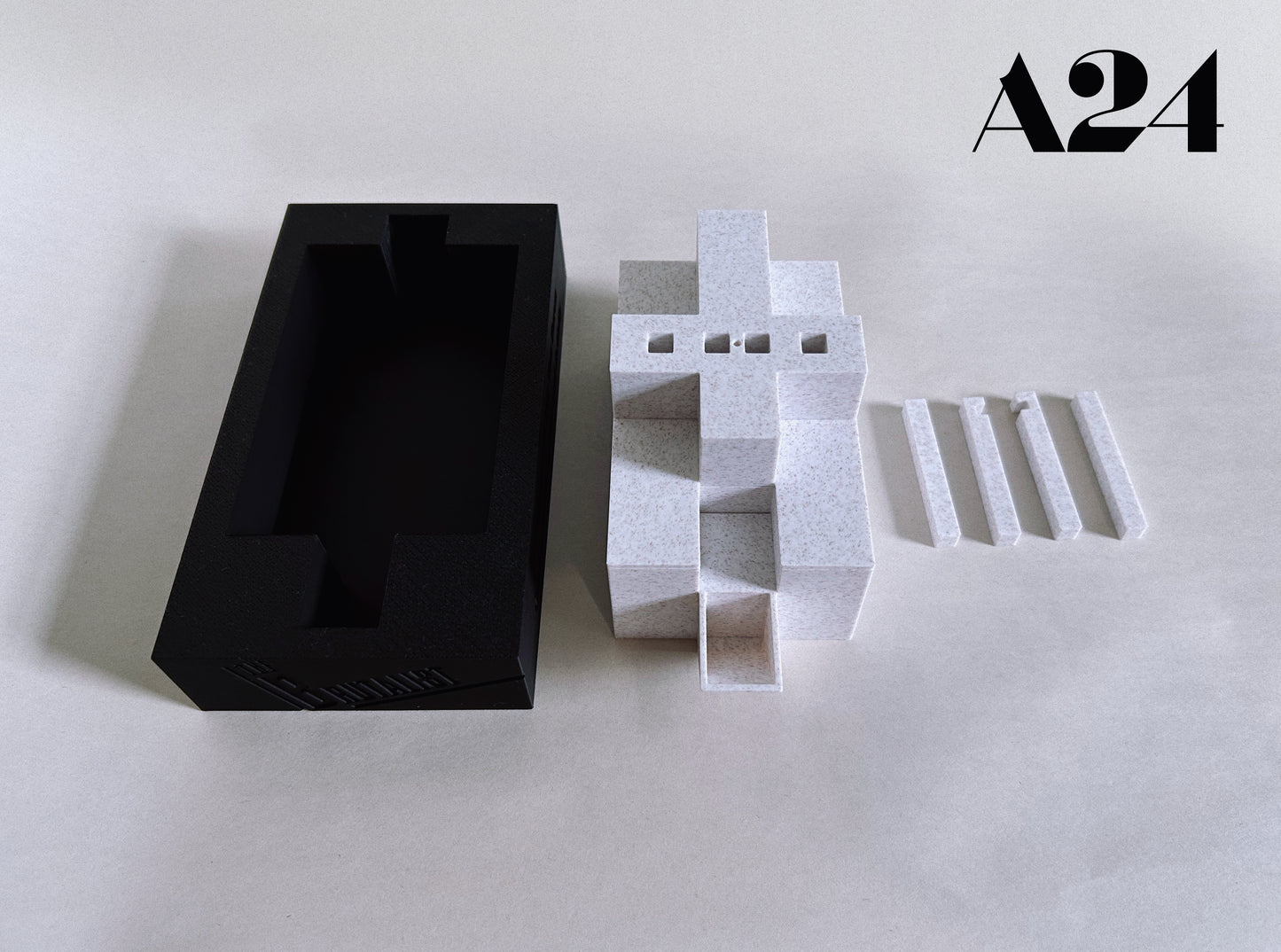 Black rectangular box and white geometric sculpture on a light gray background with 'A24' branding.