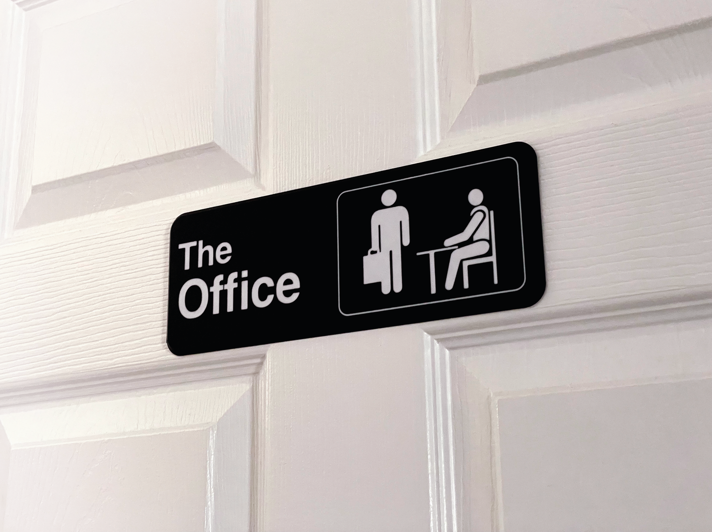 Black sign with 'The Office' text and icons on a white door.
