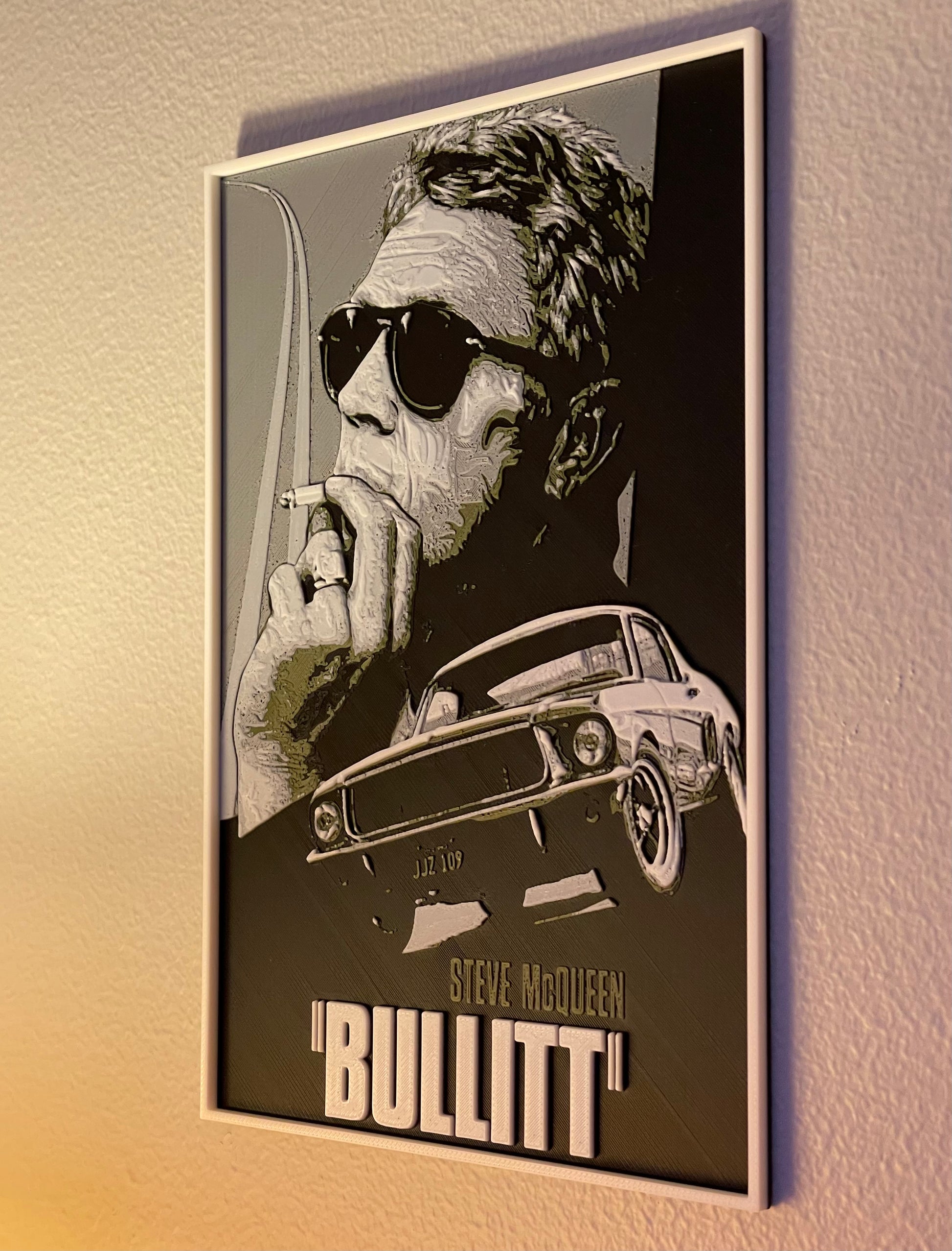 Framed poster of a stylized portrait with sunglasses and a car, featuring the text 'Bullitt' on a beige wall.