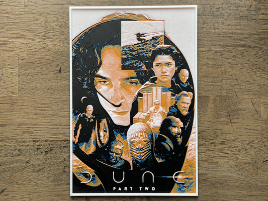 Artistic depiction of a character with multiple faces and a cityscape, titled 'Dune Part Two', on a wooden surface.