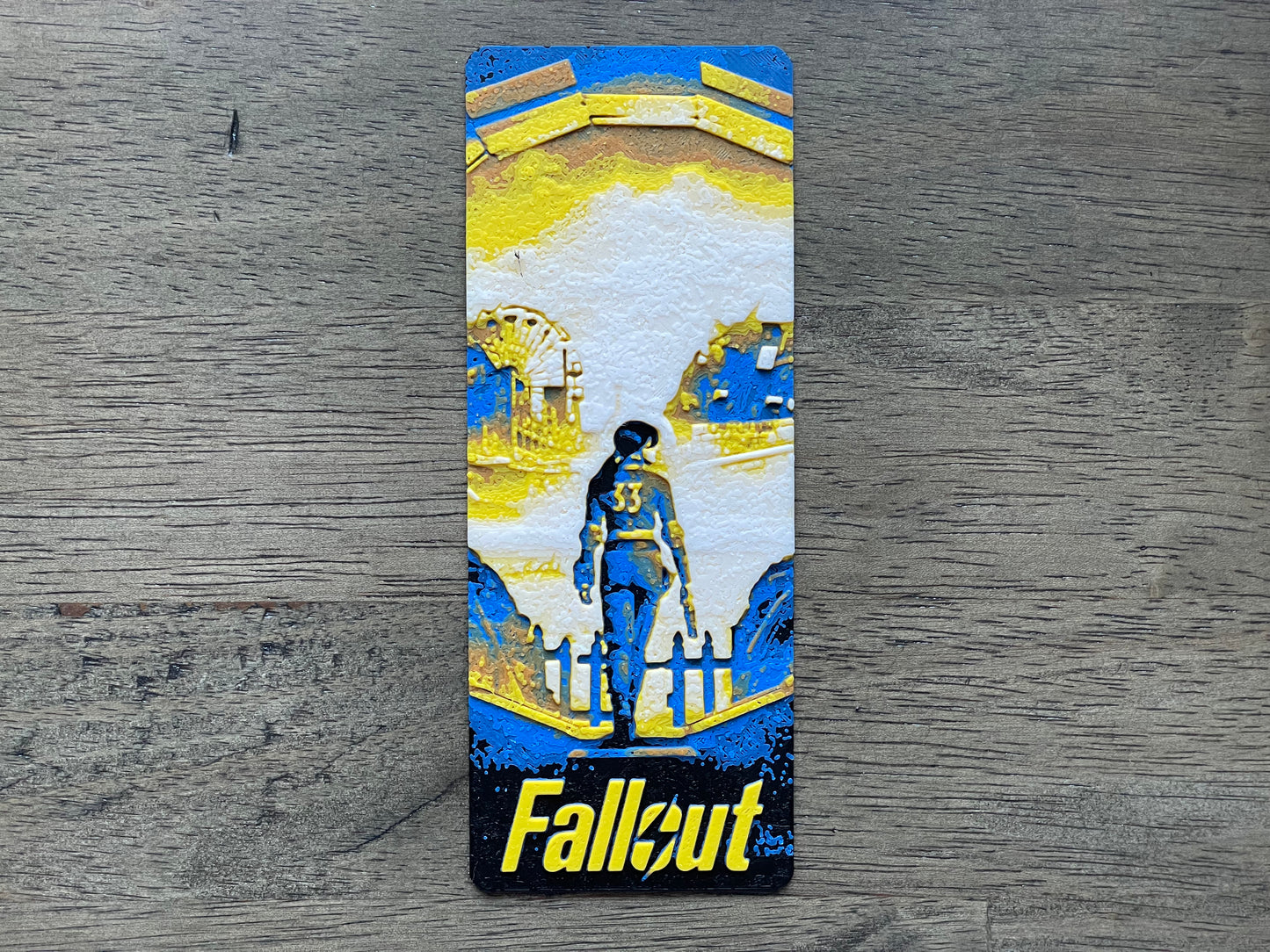 bookmark with 'Fallout' design featuring a character and architecture on a wooden surface