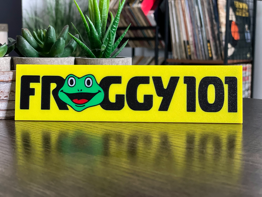 Yellow sign with a frog graphic and 'FROGGY 101' text on a wooden surface.
