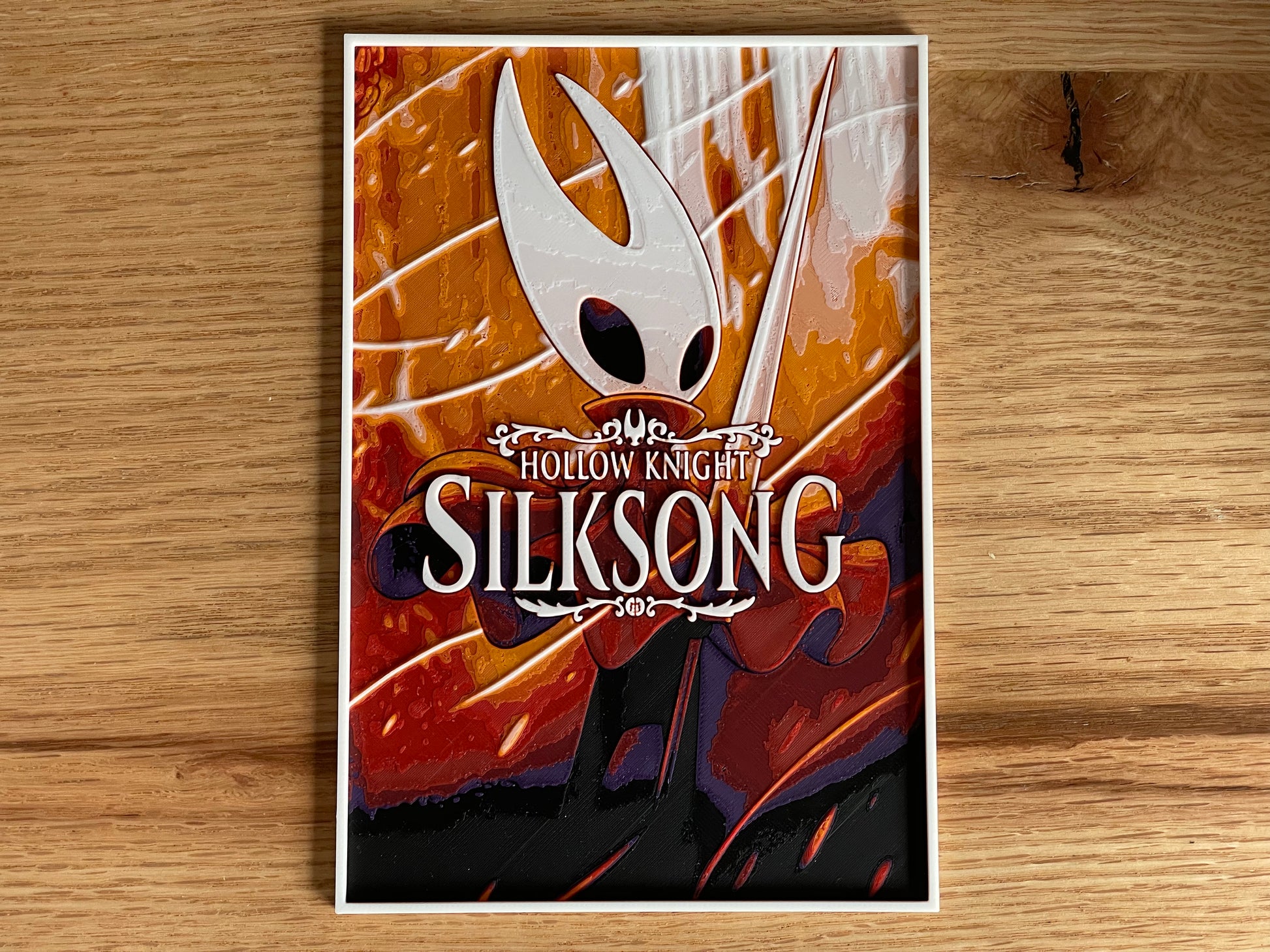 Poster of 'Hollow Knight: Silksong' with a character holding a sword on a wooden surface.