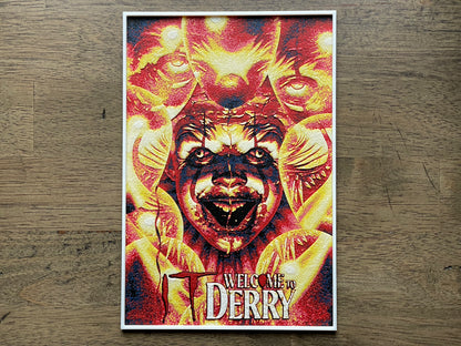 Poster of a creature with text 'Welcome to Derry' and pennywise the clown on a wooden surface