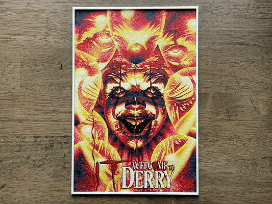 Poster of a creature with text 'Welcome to Derry' and pennywise the clown on a wooden surface