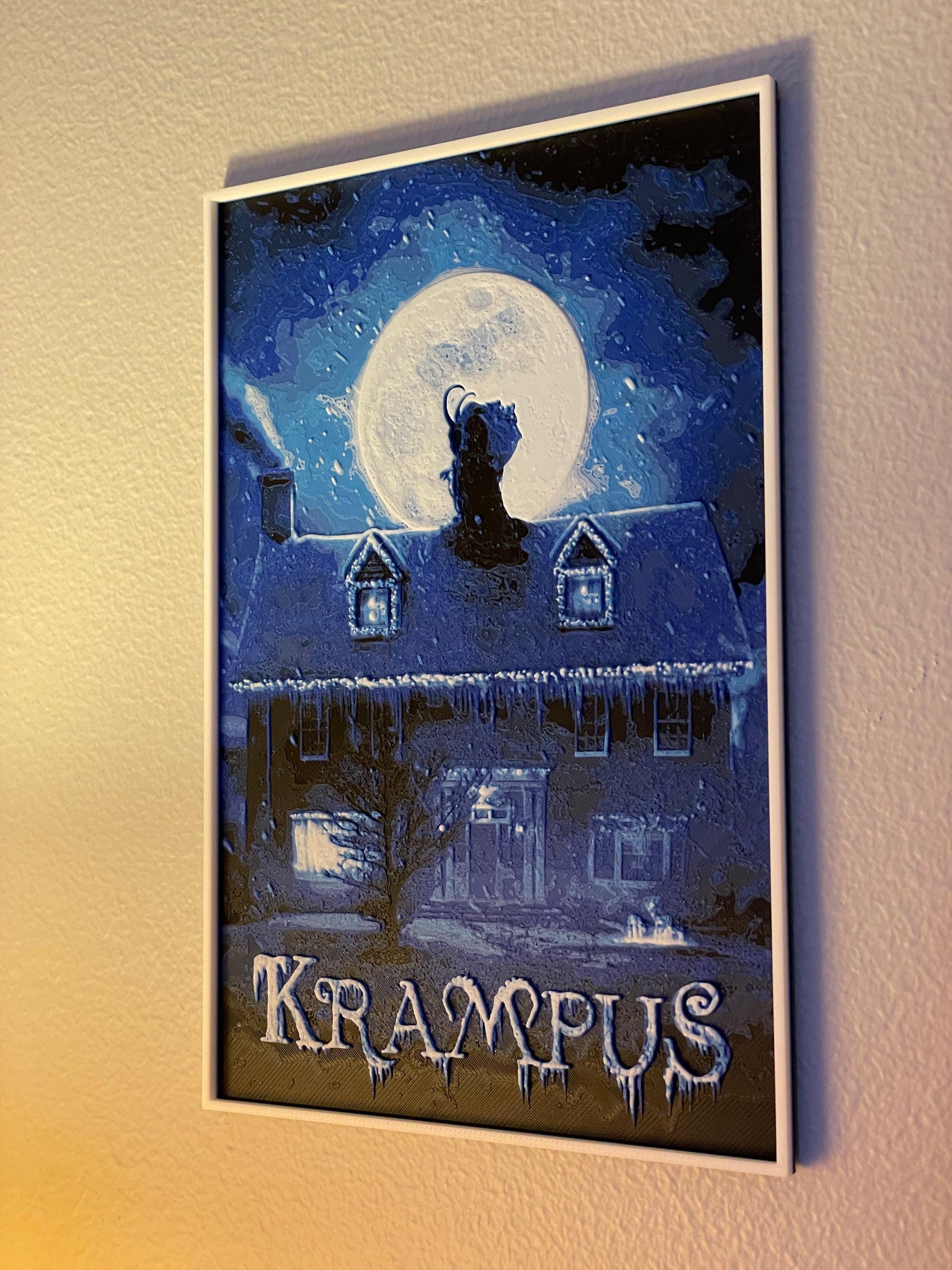 Framed Krampus poster with a house and moonlit sky on a wall.