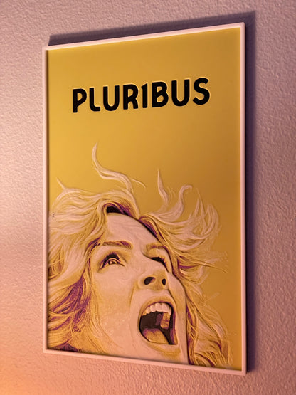 Book or notebook with a cover featuring a person's face and the word 'PLURIBUS' on a gold background.