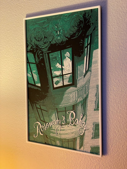 Decorative wall art with a stylized illustration of a building and window, featuring the text 'Rosemary's Baby'.