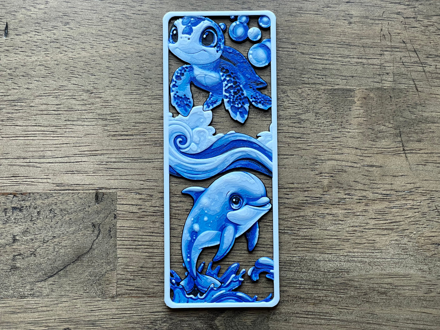 Decorative bookmark with blue dolphin design on a wooden surface