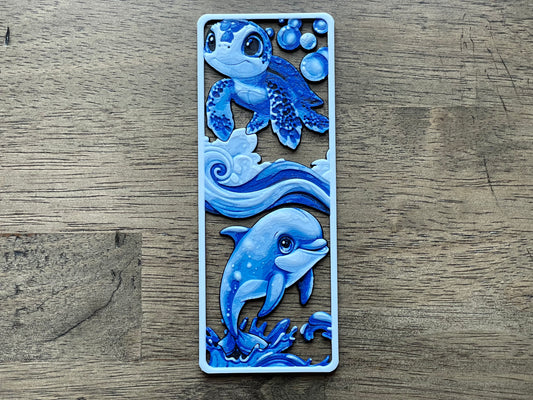 Decorative bookmark with blue dolphin design on a wooden surface