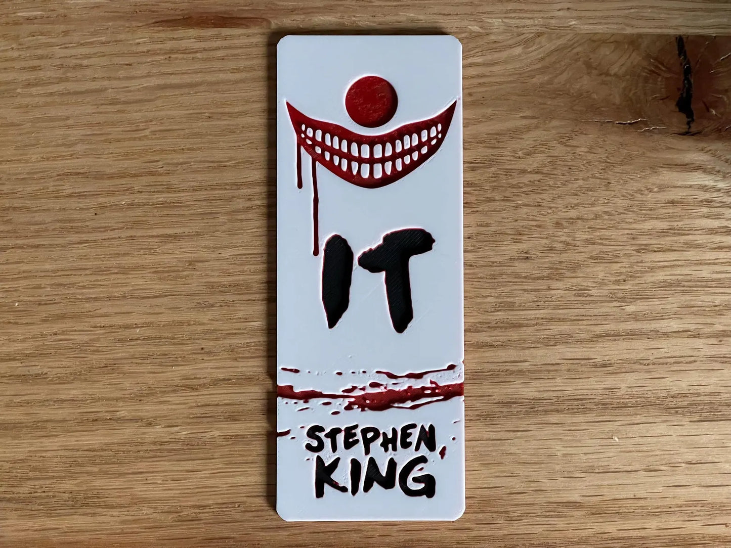 Bookmark with 'IT' by Stephen King design on a wooden surface