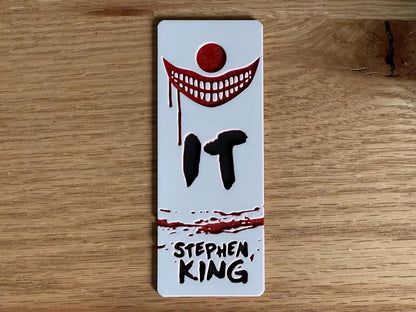 Bookmark with 'IT' by Stephen King design on a wooden surface