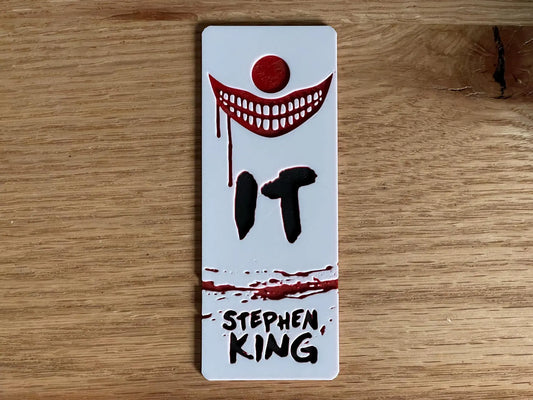 Bookmark with 'IT' by Stephen King design on a wooden surface