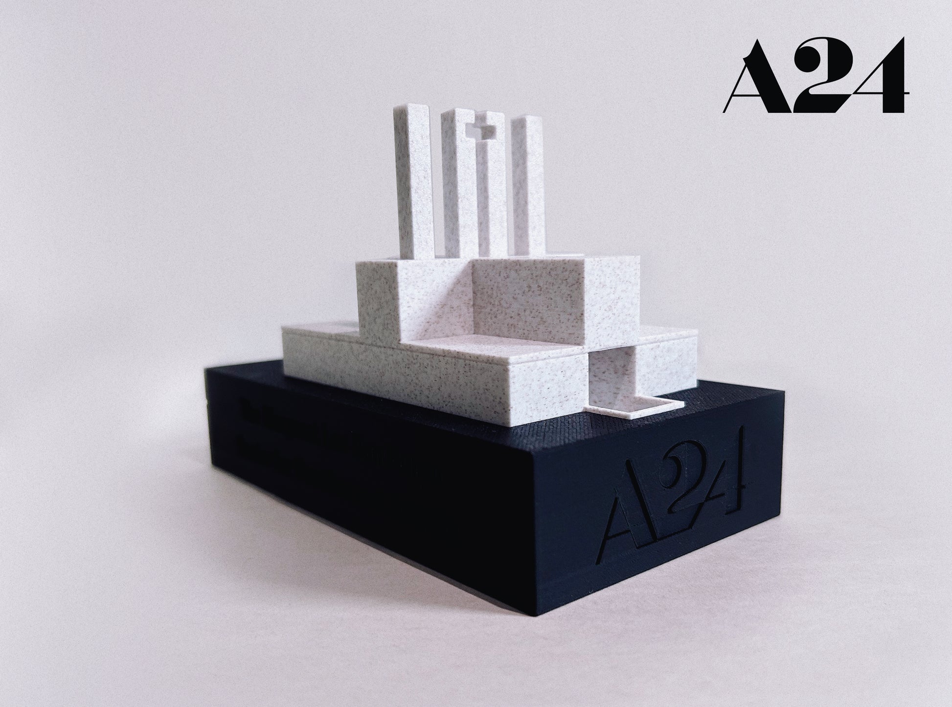 Minimalist sculpture on a black base with 'A24' branding on a light gray background