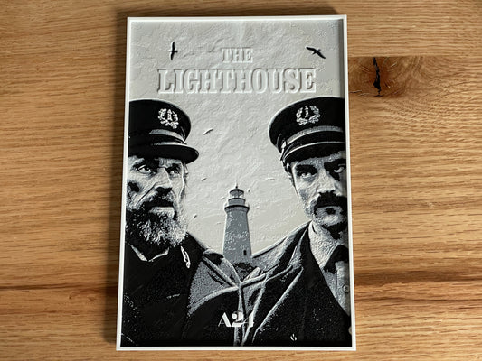 Movie poster for 'The Lighthouse' featuring two men and a lighthouse on a wooden surface.