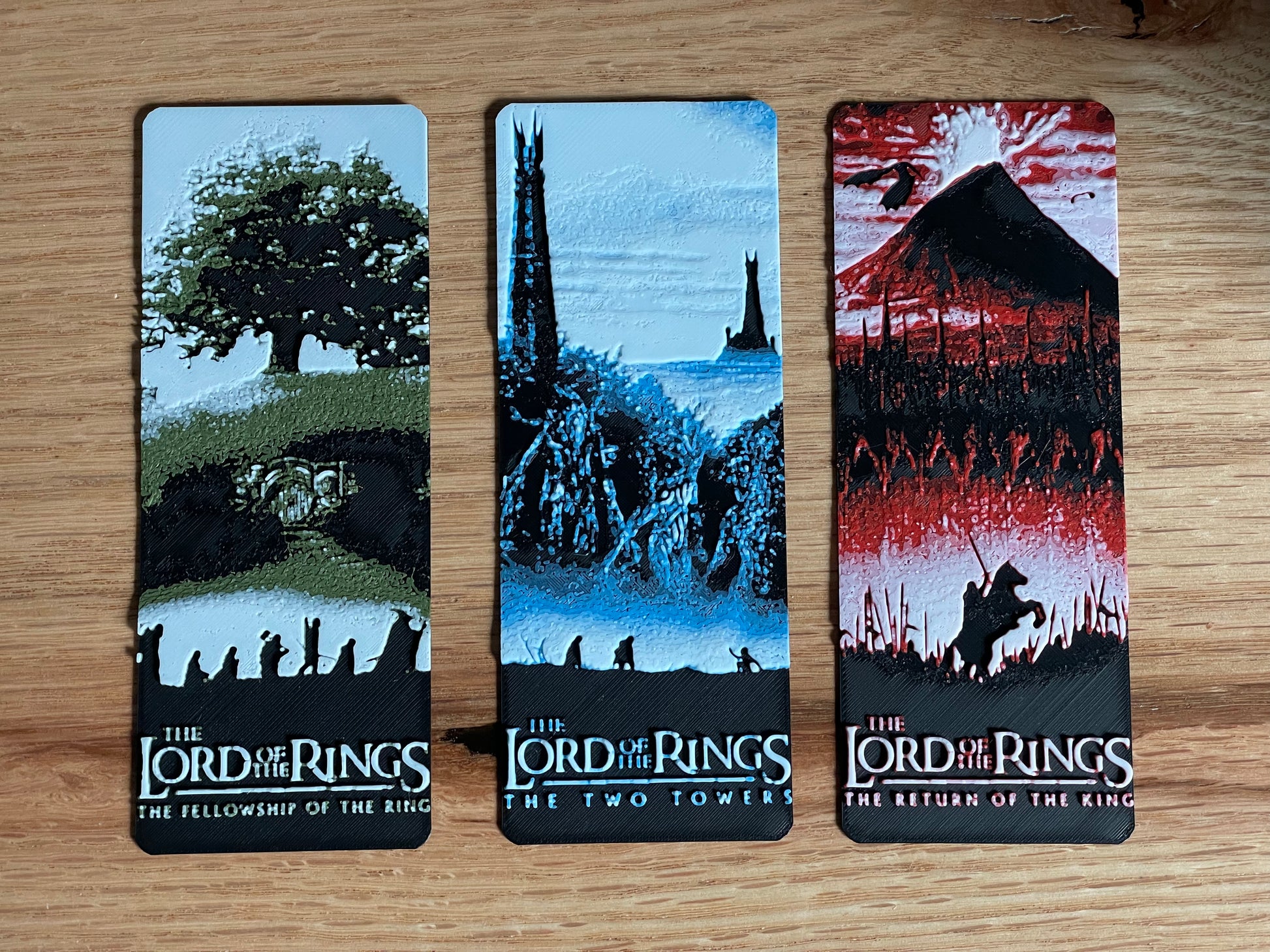 Three 'The Lord of the Rings' bookmarks on a wooden surface