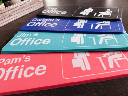 Stack of office nameplates with 'The Office' and personalized names on a wooden surface