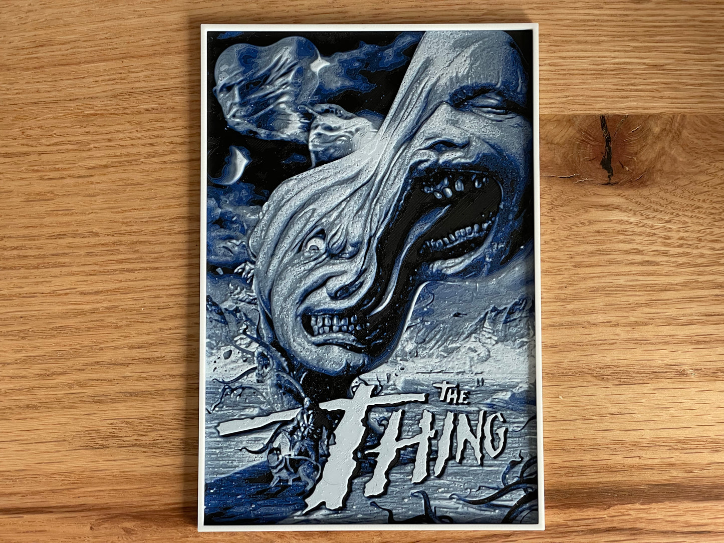 Poster of 'The Thing' with a creature's face on a wooden surface