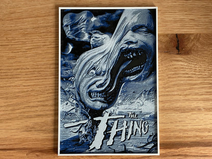 Poster of 'The Thing' with a creature's face on a wooden surface
