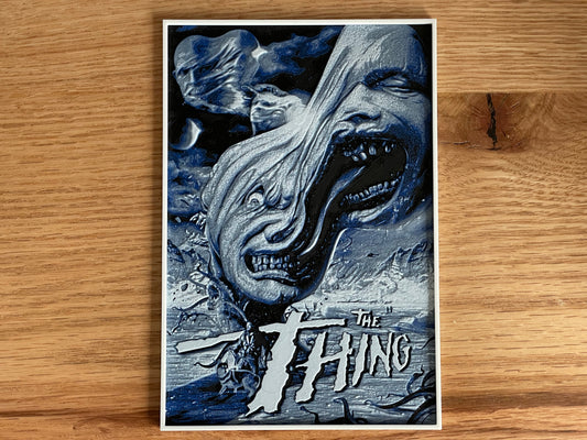 Poster of 'The Thing' with a creature's face on a wooden surface