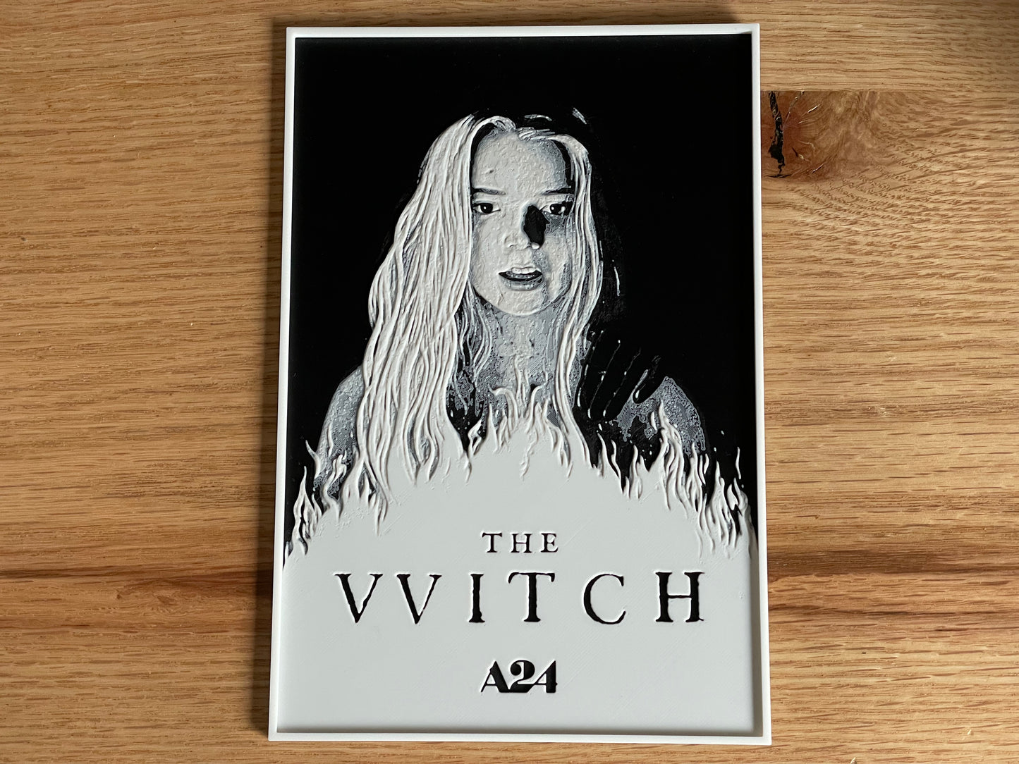 Poster of 'The VVitch' with a black and white illustration on a wooden surface